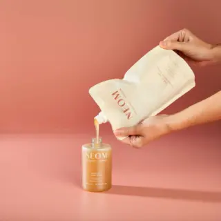 Hands pouring liquid from refill pouch into NEOM hand wash bottle.