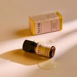 Neom essential oil bottle with box, oil spilled on a beige surface.