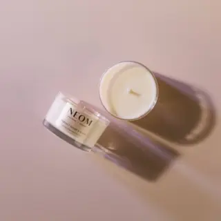 Two NEOM candles on a beige surface, one with a lid and one open.