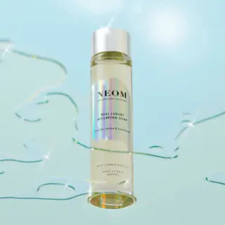 NEOM Real Luxury Wellbeing Soak bottle with shimmering water background.