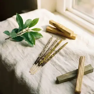 Incense sticks, wooden blocks, and green leaves on a linen cloth by a window.