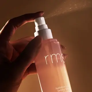 Hand spraying rms Radiance Lock Setting Mist in warm lighting.