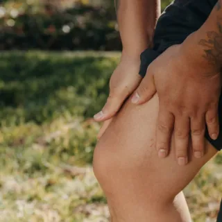 Person holding their knee outdoors, grass in the background.