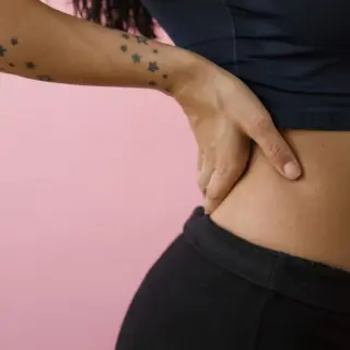 Person with star tattoos holding their waist against a pink background.