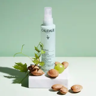 Caudalie cleansing oil bottle with almonds and grape on a white block.