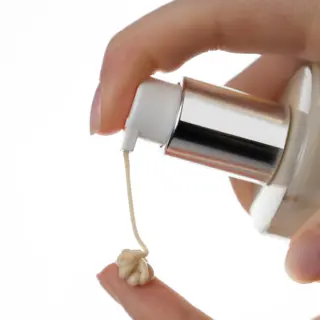 Hand dispensing cream onto fingertip from a pump bottle.