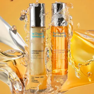 Two bottles of The Organic Pharmacy antioxidant gel and serum with liquid splash on orange background.