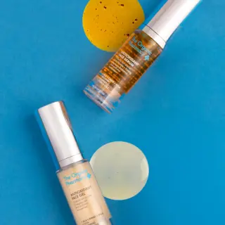 Two skincare bottles on blue background with yellow gel samples.