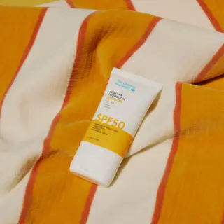 SPF 50 sunscreen tube on a striped orange and white fabric background.