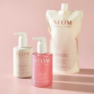 NEOM Complete Bliss hand wash, lotion, and refill pouch on a pink background.