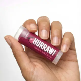 Hand holding Hurraw! raspberry tinted lip balm.
