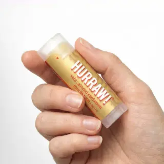 Hand holding Hurraw! almond cardamom rose lip balm tube.