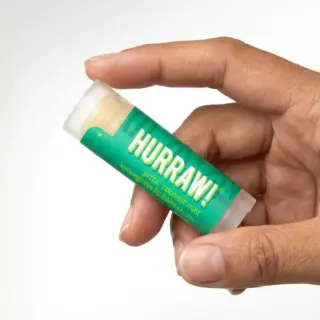 Hand holding Hurraw! lemongrass lip balm tube.