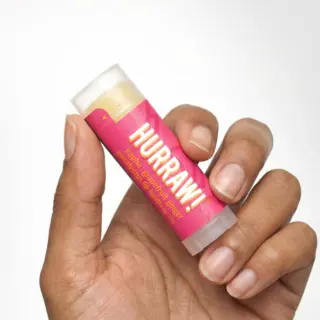 Hand holding pink Hurraw! lip balm tube.