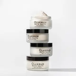 Stack of four Olverum bath salts jars with black lids on a white background.