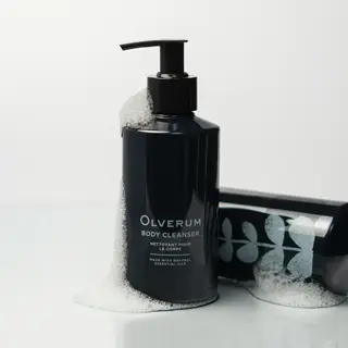 Dark bottle of Olverum body cleanser with foam, next to a matching tube.