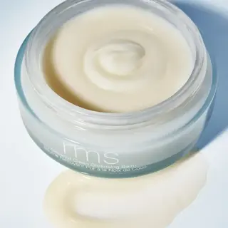 Open jar of rms coconut cleansing balm with some balm spilled on surface.