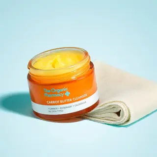 Orange jar of Carrot Butter Cleanser with cloth on blue background.