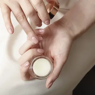 Hands holding a small jar of cream, with fingers applying it.