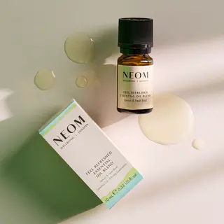 NEOM Feel Refreshed essential oil blend bottle and box on a light surface with oil droplets.