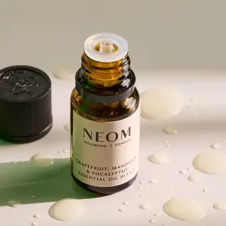 Open bottle of NEOM essential oil with drops on a surface.