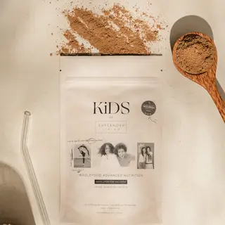 KiDS wholefood nutrition powder with spoon, straw, and spilled powder on a light surface.