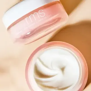 Open jar of RMS cream with white lid and smooth cream inside, on a beige background.