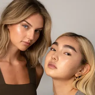 Two women with glowing skin, one with long blonde hair, the other with short blonde hair and earrings.