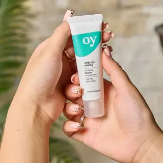 Hands holding a tube of "oy" purifying serum for clear skin.