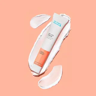 Lip and eye cream tube on peach background with cream smears.