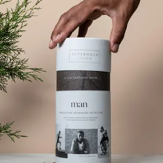 Hand reaching for Supernova Living nutrition drink container on table with cocoa beans.