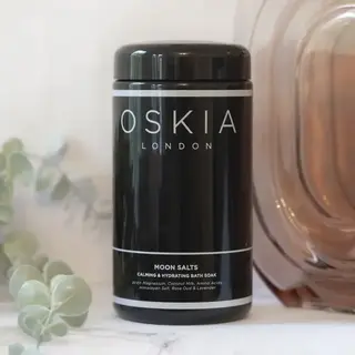 Oskia London Moon Salts jar on marble surface with eucalyptus leaves.