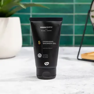 Black tube of Green People Energising Shower Gel on a white surface. Green tiled background.