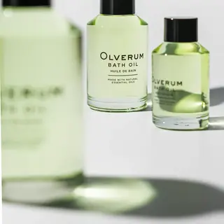 Olverum Bath Oil bottles with green liquid and black caps. Text: "Made with natural essential oils".