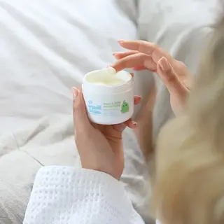Hand applying Organic Babies mum & baby rescue balm from a white jar.