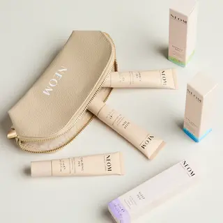 Beige pouch with NEOM logo, surrounded by NEOM skincare tubes and boxes on a light surface.