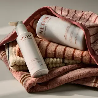 NEOM body lotion and cream on folded striped towels.