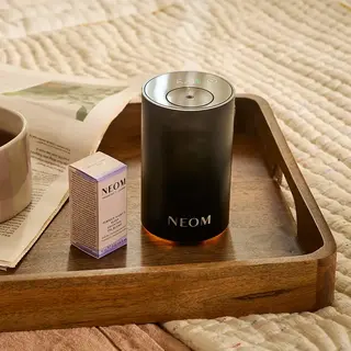 NEOM diffuser and oil box on a wooden tray with a cup and newspaper.