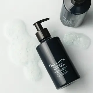 Dark bottle of Olverum Purifying Hand Wash with foam on a white surface.