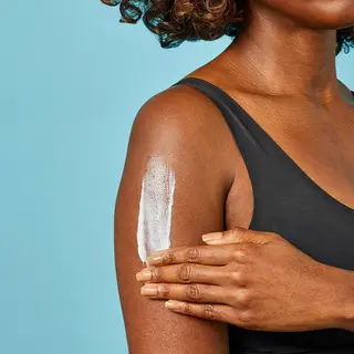 Woman applying lotion to her arm against a blue background.