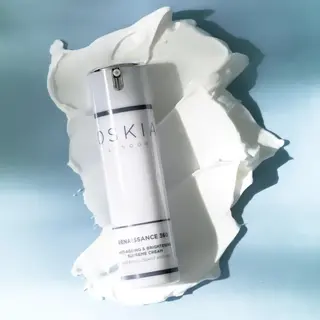 Oskia Renaissance 360 cream bottle on white cream smear, blue background.
