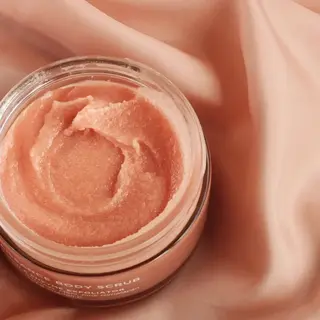 Open jar of pink body scrub on a silky pink fabric background.