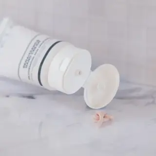 White skincare tube open on marble surface, cream squeezed out.