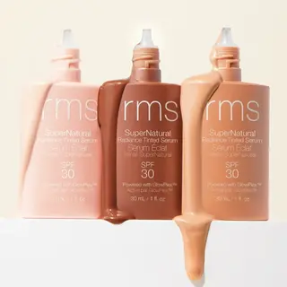Three bottles of rms SuperNatural Radiance Tinted Serum SPF 30 in different shades.