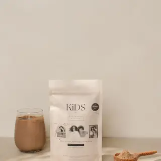 Kids nutrition powder with glass of chocolate drink and wooden scoop on a beige surface.