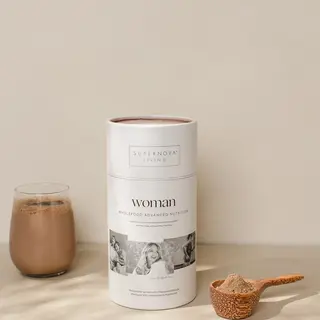 Supernova Living Woman supplement with a glass of chocolate drink and a wooden scoop of powder.