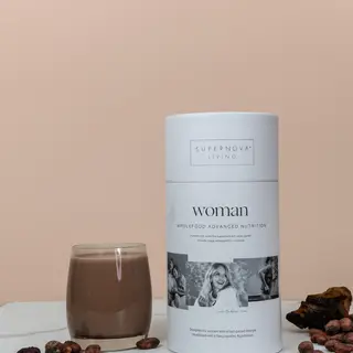 Supernova Living Woman nutrition powder with a glass of chocolate drink on a marble surface.