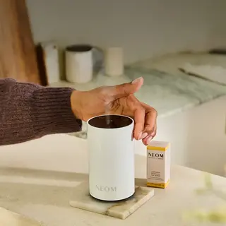 Hand adjusting a NEOM diffuser on a marble surface, with a NEOM oil blend box nearby.