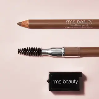 Brown eyebrow pencil, spoolie brush, and sharpener on a light pink background. Text: "rms beauty".