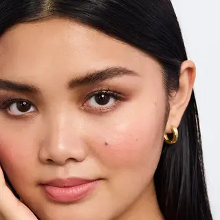 Close-up of a person with smooth skin, wearing gold hoop earrings. Text: "Shade Dark".